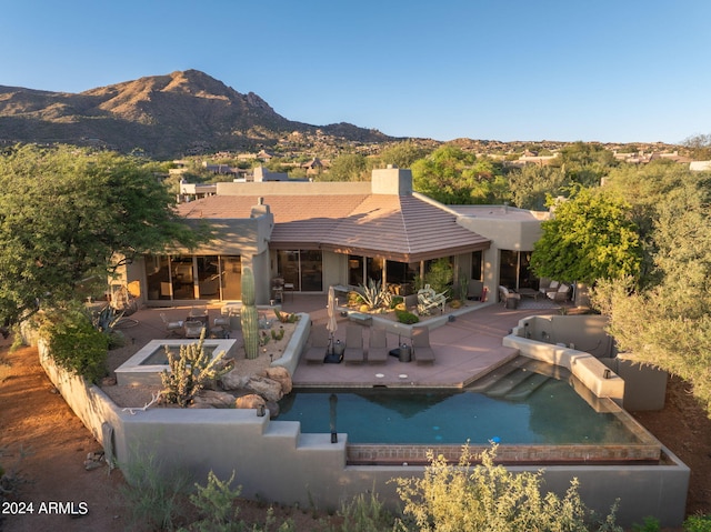 back of house with a swimming pool with hot tub, a mountain view, and a patio area