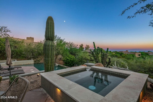 pool at dusk featuring an in ground hot tub