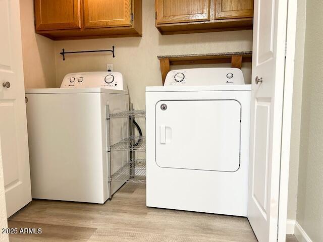 laundry room with cabinet space, washing machine and dryer, and light wood finished floors