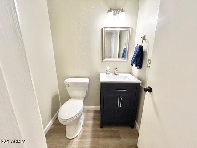 half bath featuring baseboards, toilet, wood finished floors, and vanity