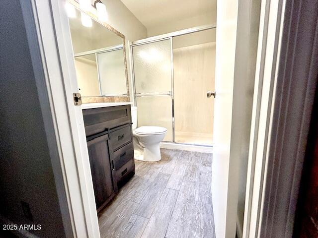 full bath featuring vanity, a shower stall, toilet, and wood finished floors