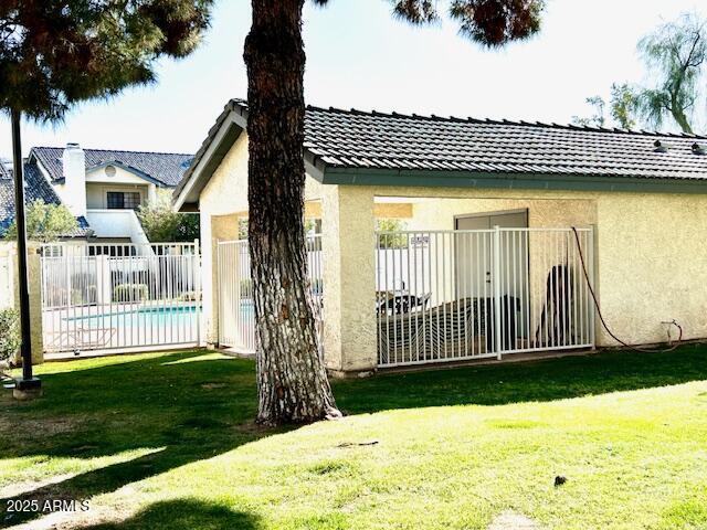 view of property exterior featuring a tile roof, stucco siding, a lawn, and fence