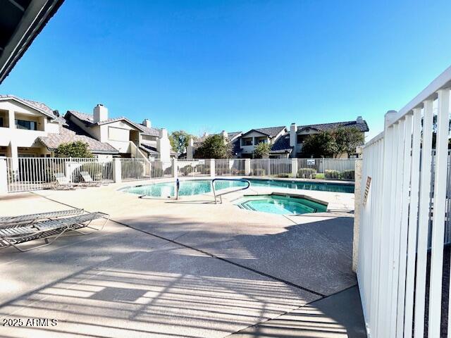 community pool with a patio area, a hot tub, and fence