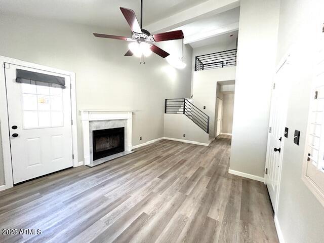 unfurnished living room featuring baseboards, stairway, a fireplace, wood finished floors, and a ceiling fan