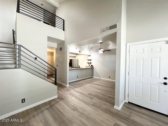 unfurnished living room with visible vents, baseboards, stairway, wood finished floors, and a ceiling fan