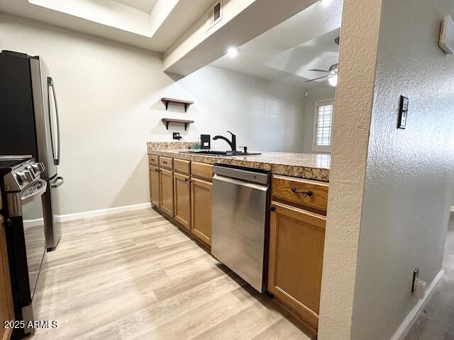 kitchen featuring light wood-style floors, brown cabinetry, baseboards, stove, and dishwasher