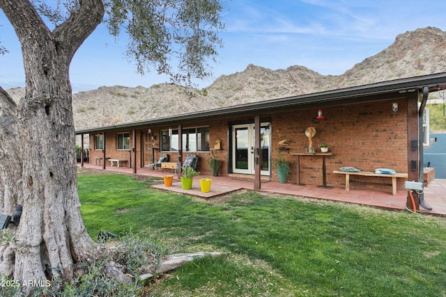 back of property with french doors, brick siding, a patio, a lawn, and a mountain view