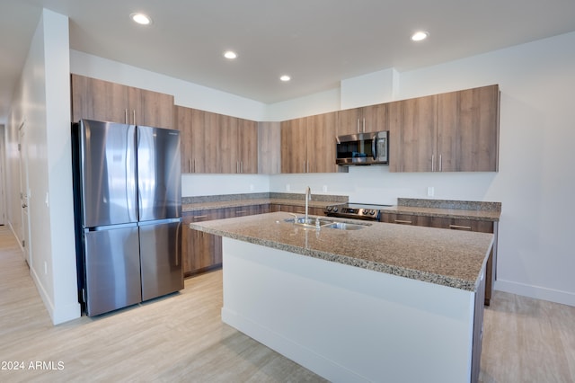 kitchen featuring light hardwood / wood-style flooring, an island with sink, stainless steel appliances, light stone countertops, and sink