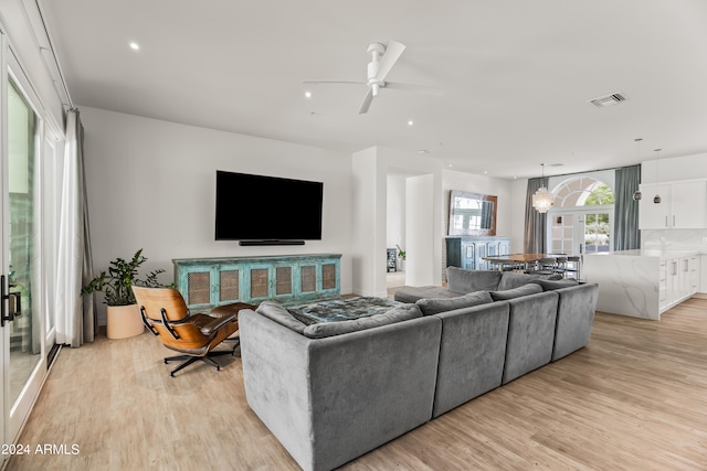 living room with ceiling fan with notable chandelier and light hardwood / wood-style floors