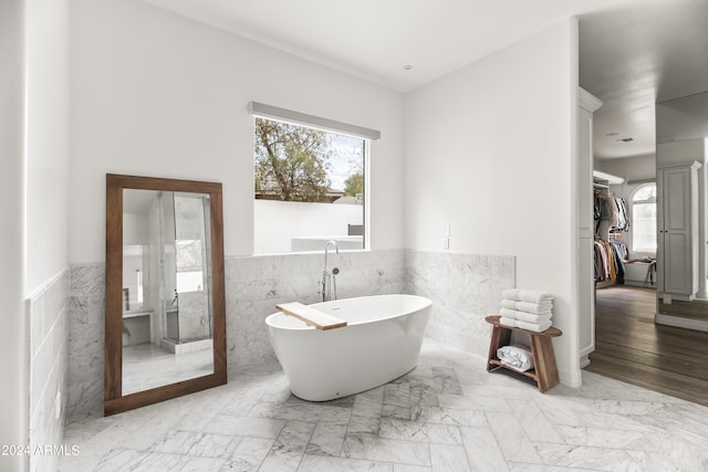 bathroom with a tub to relax in and tile walls