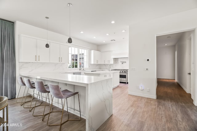 kitchen featuring kitchen peninsula, high end stove, decorative light fixtures, white cabinets, and hardwood / wood-style floors