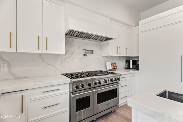 kitchen featuring double oven range, light wood-type flooring, tasteful backsplash, light stone counters, and white cabinetry