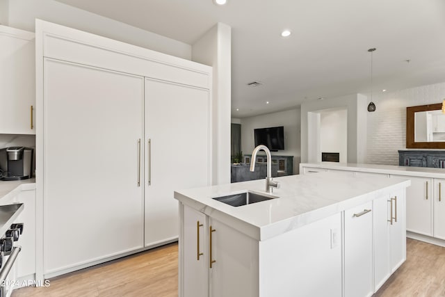 kitchen featuring light wood-type flooring, white cabinetry, sink, and a kitchen island with sink