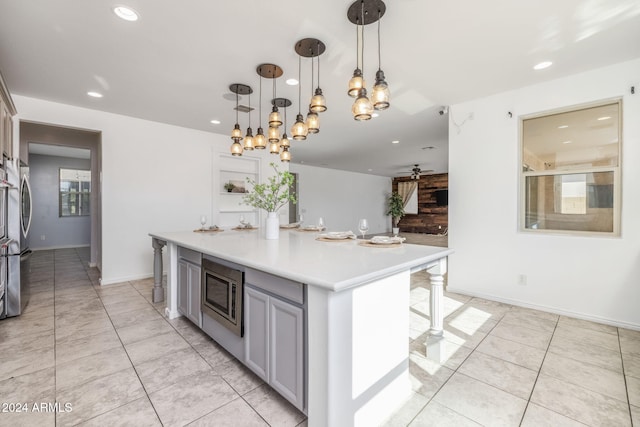 kitchen featuring gray cabinetry, a center island, stainless steel appliances, a kitchen breakfast bar, and pendant lighting