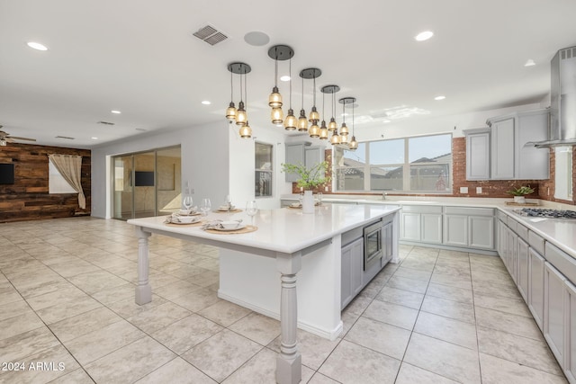 kitchen featuring tasteful backsplash, gray cabinets, wood walls, and wall chimney exhaust hood