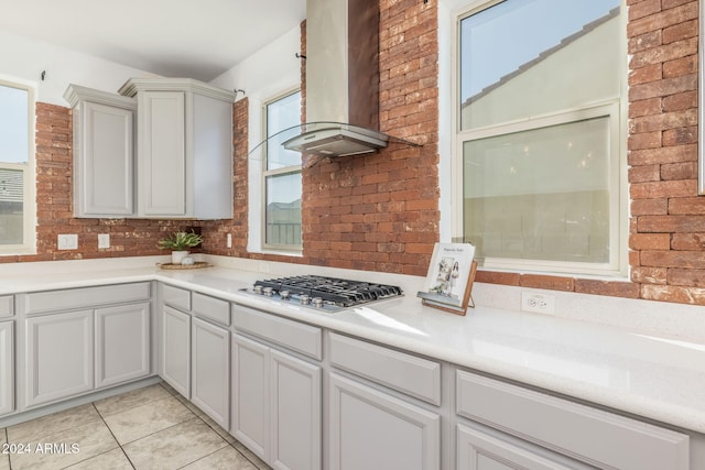 kitchen with light tile patterned floors, stainless steel gas stovetop, and wall chimney range hood