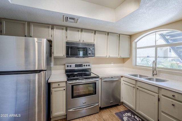 kitchen with a textured ceiling, stainless steel appliances, light hardwood / wood-style floors, and sink