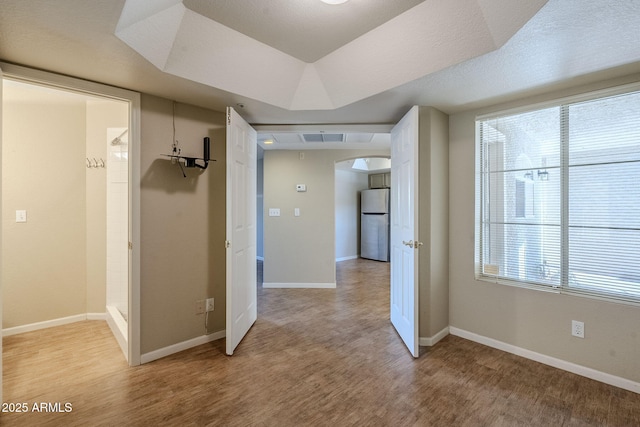 hallway with a tray ceiling and light hardwood / wood-style flooring