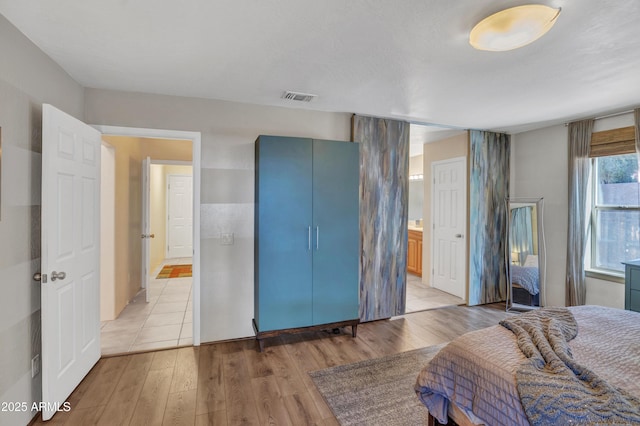 bedroom with visible vents, light wood-style flooring, and ensuite bath