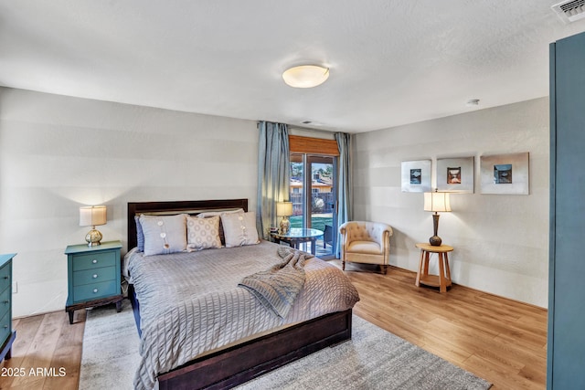 bedroom featuring access to outside, visible vents, and wood finished floors