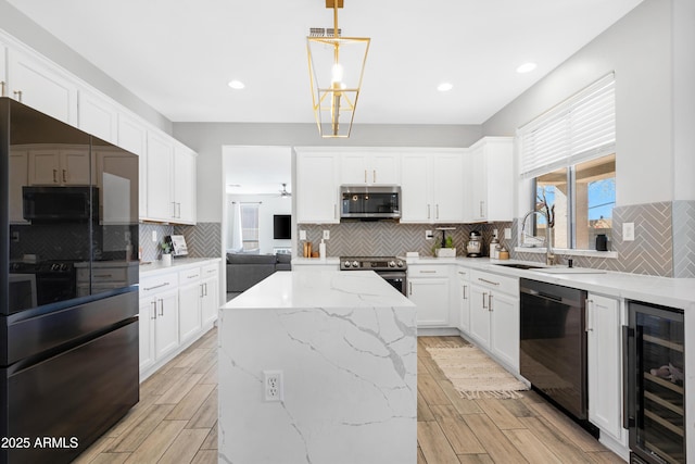 kitchen featuring white cabinets, beverage cooler, black appliances, a kitchen island, and hanging light fixtures