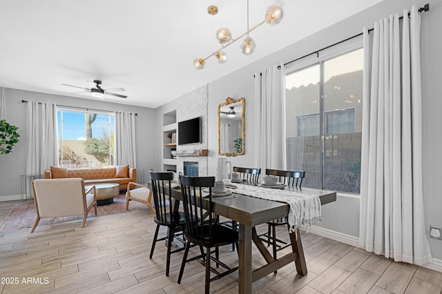 dining area with ceiling fan, a large fireplace, built in features, and a healthy amount of sunlight