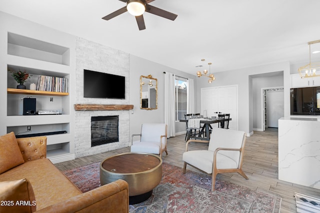 living room featuring built in features, ceiling fan with notable chandelier, and a large fireplace