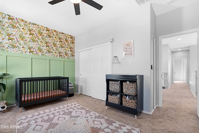 bedroom featuring ceiling fan, a nursery area, and light colored carpet