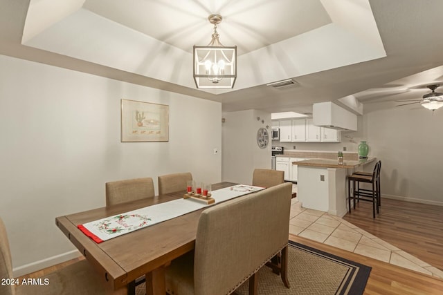 dining room featuring ceiling fan with notable chandelier, a tray ceiling, and light hardwood / wood-style flooring