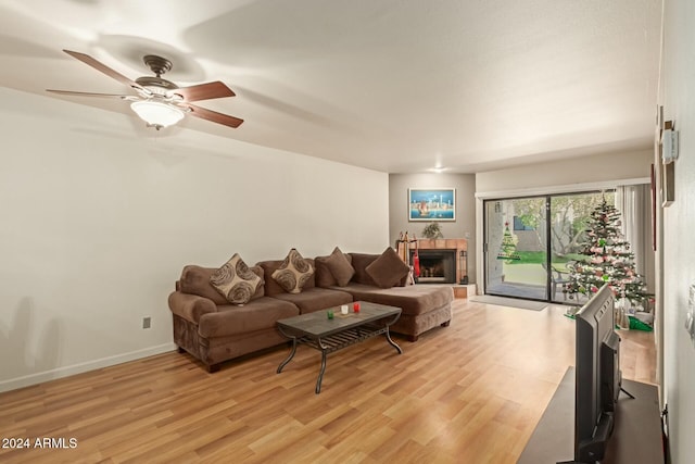 living room with a tile fireplace, ceiling fan, and light wood-type flooring