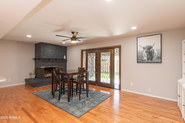 dining area with baseboards, light wood-style floors, french doors, and a brick fireplace