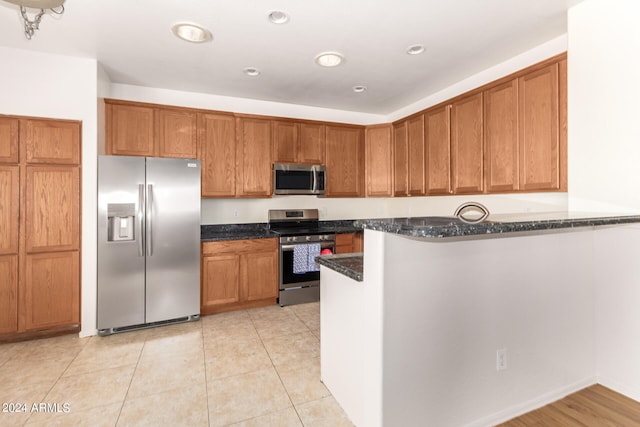 kitchen featuring dark stone countertops, light tile patterned floors, stainless steel appliances, and kitchen peninsula