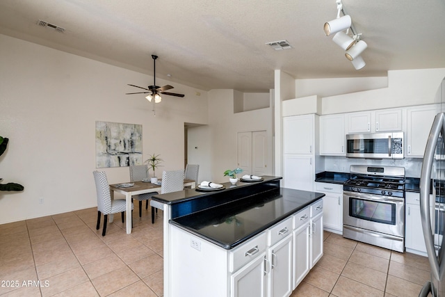 kitchen featuring stainless steel appliances, white cabinetry, lofted ceiling, and light tile patterned flooring