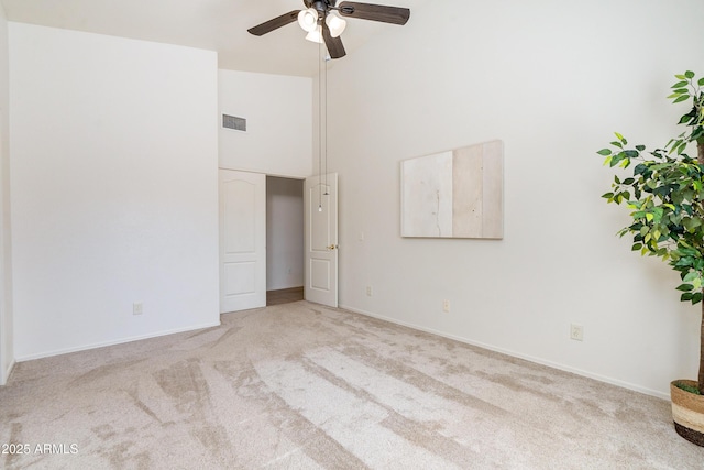 unfurnished room featuring a towering ceiling, light colored carpet, and ceiling fan