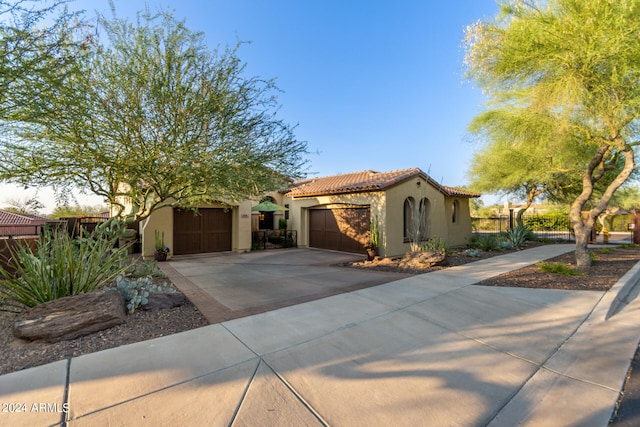 mediterranean / spanish-style home featuring driveway, a tiled roof, an attached garage, fence, and stucco siding