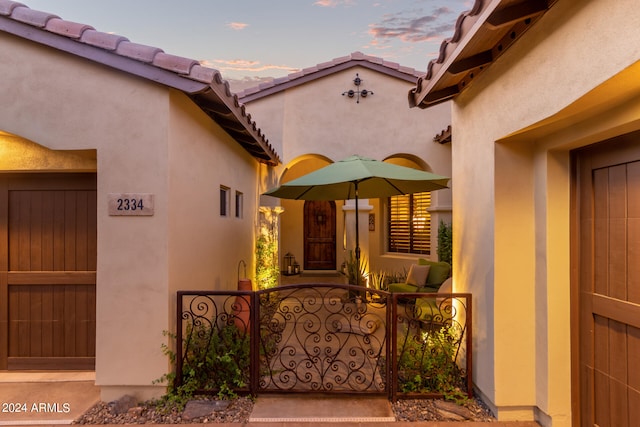 exterior entry at dusk with a tile roof, a gate, and stucco siding