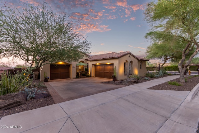 mediterranean / spanish home with a garage, fence, a tiled roof, driveway, and stucco siding