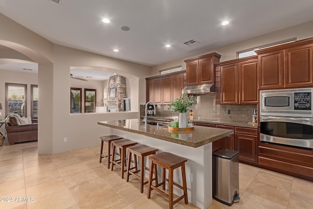 kitchen featuring sink, tasteful backsplash, a center island with sink, stainless steel appliances, and a kitchen bar