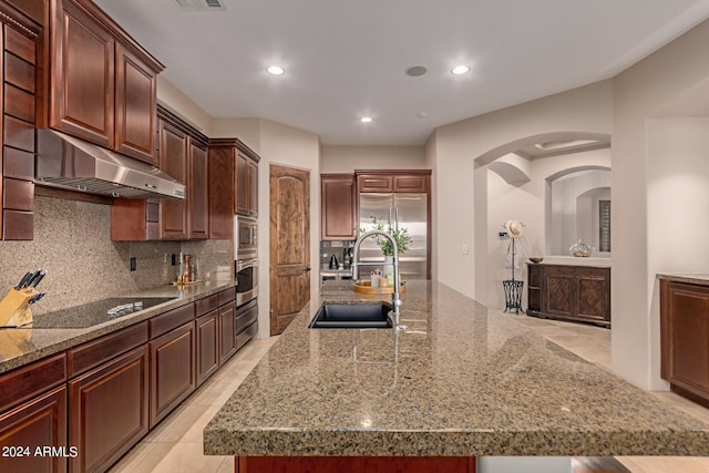 kitchen featuring arched walkways, under cabinet range hood, a sink, appliances with stainless steel finishes, and decorative backsplash