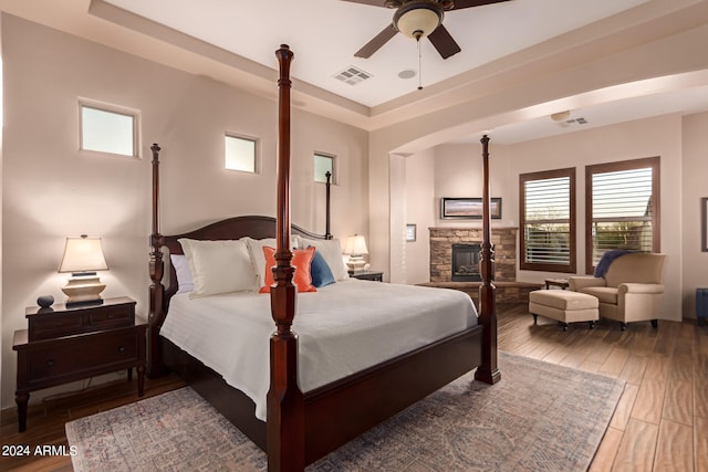 bedroom with ceiling fan, a fireplace, a raised ceiling, and wood-type flooring