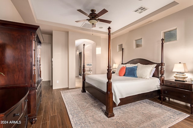 bedroom with arched walkways, ceiling fan, visible vents, dark wood-style floors, and a raised ceiling