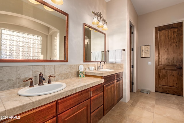 full bath with tasteful backsplash, tile patterned flooring, a sink, and double vanity