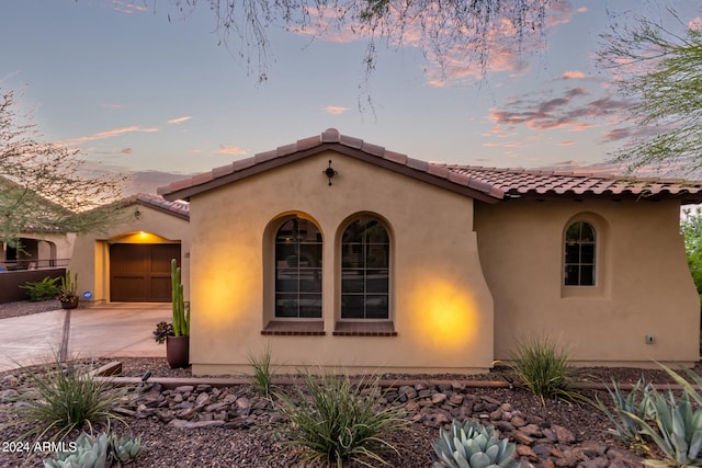 mediterranean / spanish-style house featuring an attached garage, a tiled roof, concrete driveway, and stucco siding