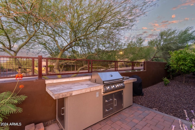 patio terrace at dusk with a grill, area for grilling, and fence