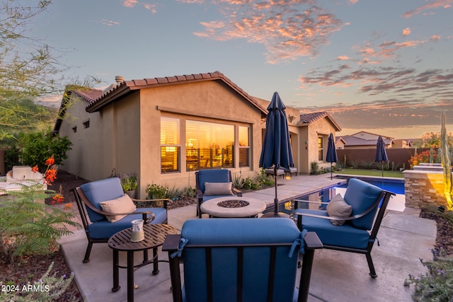 patio terrace at dusk featuring a fenced in pool and a fire pit