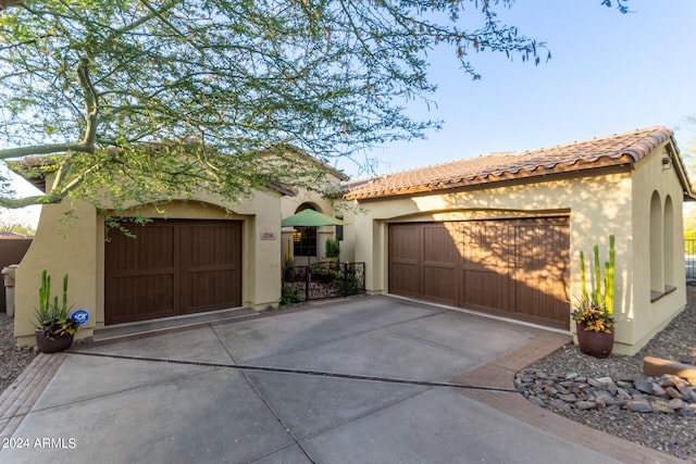 mediterranean / spanish house featuring driveway, a tiled roof, an attached garage, and stucco siding