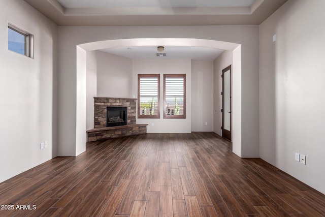 unfurnished living room featuring arched walkways, dark wood-style flooring, visible vents, and a fireplace