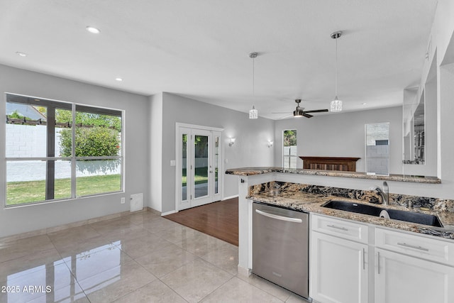 kitchen with stainless steel dishwasher, white cabinetry, light stone counters, a sink, and light tile patterned floors