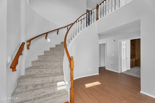 staircase with baseboards, a high ceiling, and wood finished floors
