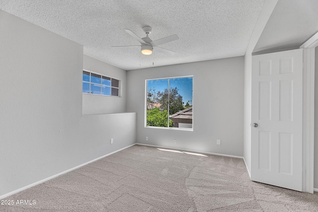 empty room with carpet flooring, a ceiling fan, a textured ceiling, and baseboards